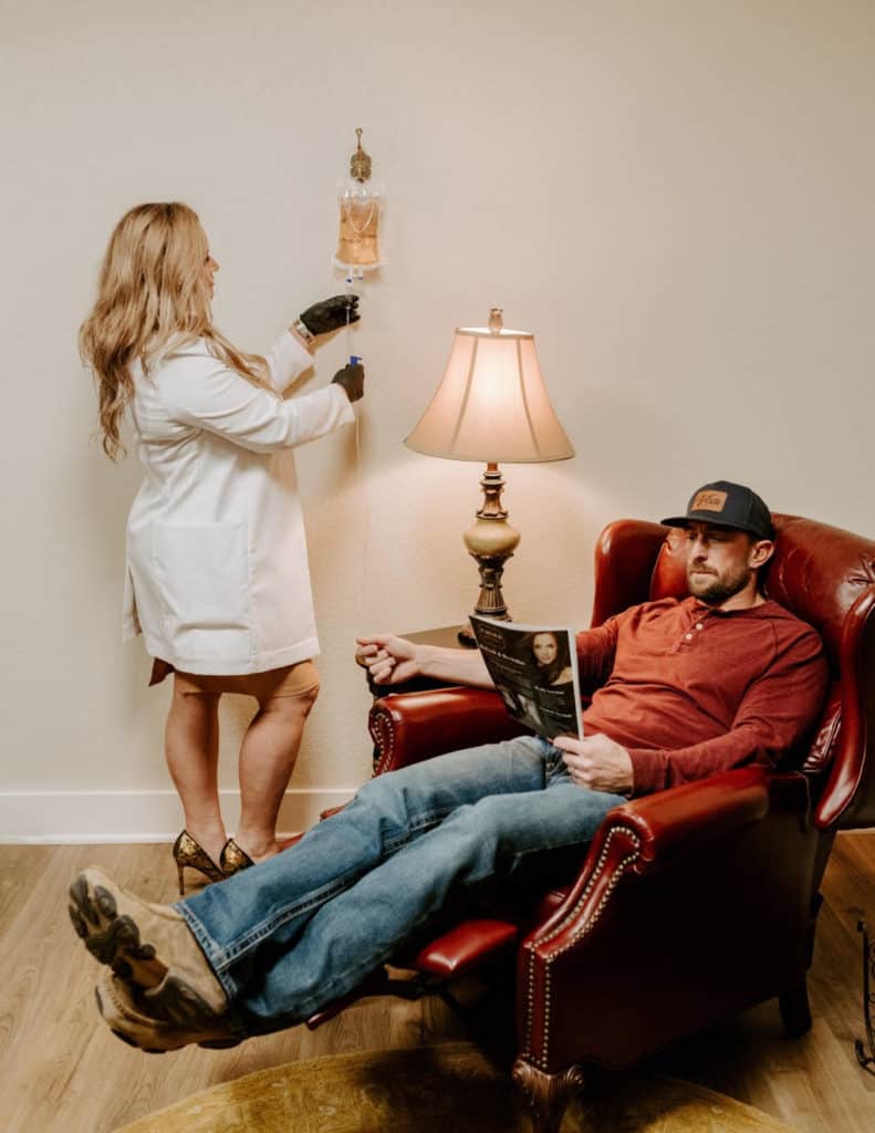 Portfolio 4 Shot of cosmetologist making IV Hydration Therapy injection with syringe for rejuvenation on the spa center man sitting on sofa reading Skin Brouchure | Parlour at the Village in Salado, TX