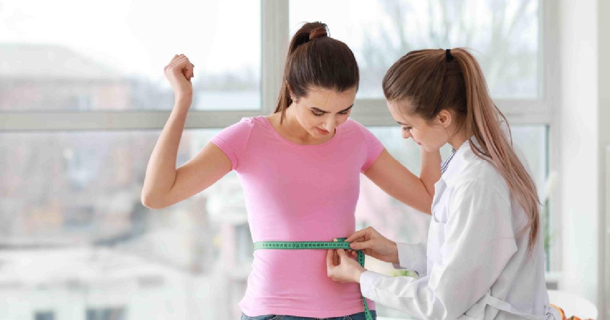 Female doctor measuring a young woman’s waist with a tape measure during a weight loss or health checkup in Salado, TX