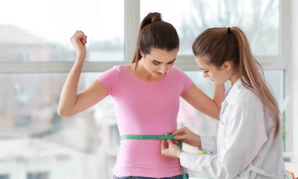 Female doctor measuring a young woman’s waist with a tape measure during a weight loss or health checkup in Salado, TX